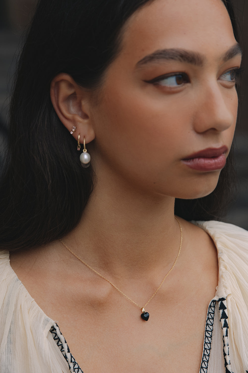 Kvinde med hjertevedhæng til halskæder med sort ædelsten og diamant og øreringe i ægte guld med ferskvandsperler fra Carré Jewellery