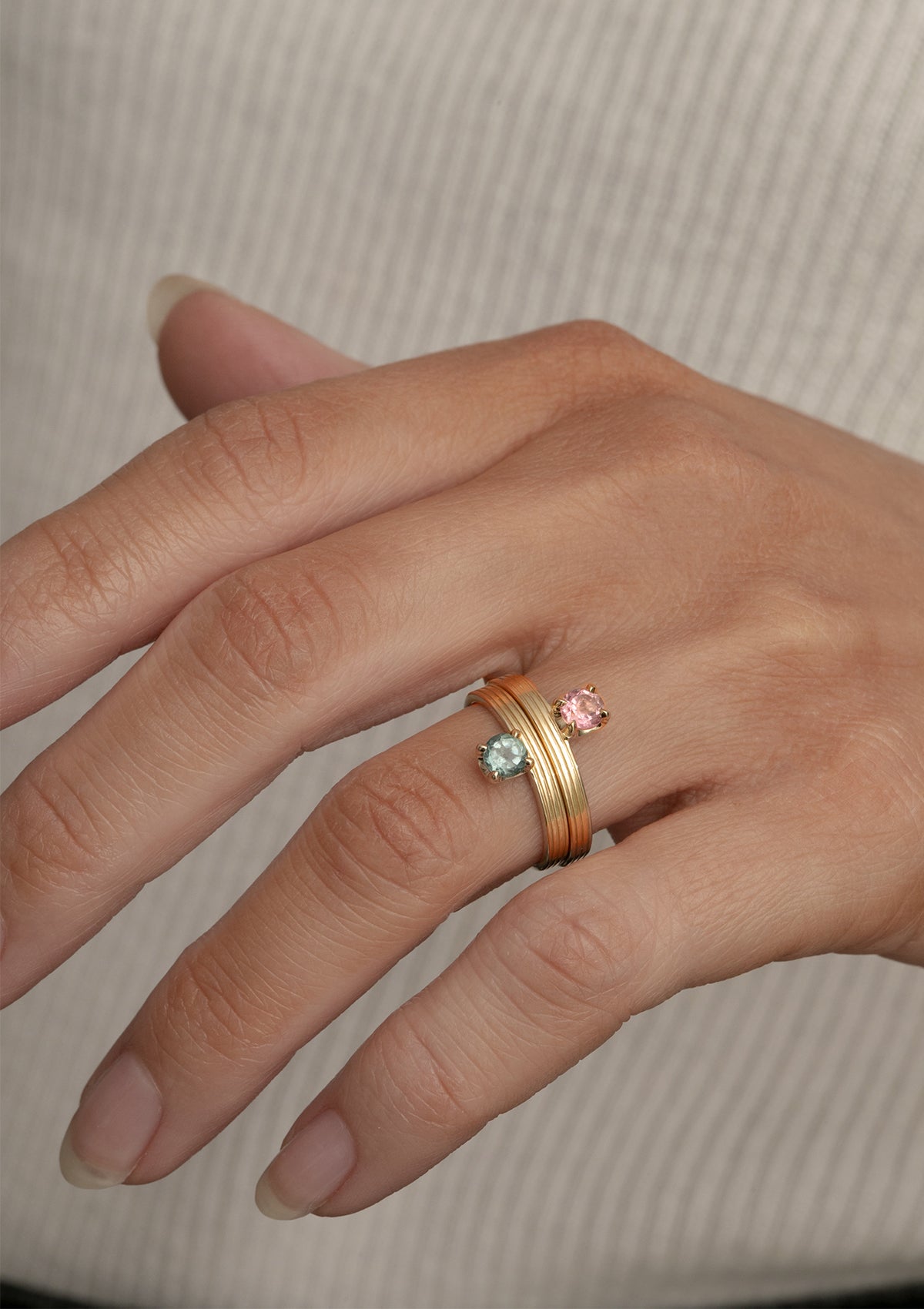 Kvindehånd med to ringe i 10-karat guld fra Carré sat med en lyserød og en grøn sten. Begge sten er Turmaliner, hvilket er oktober måneds fødselssten