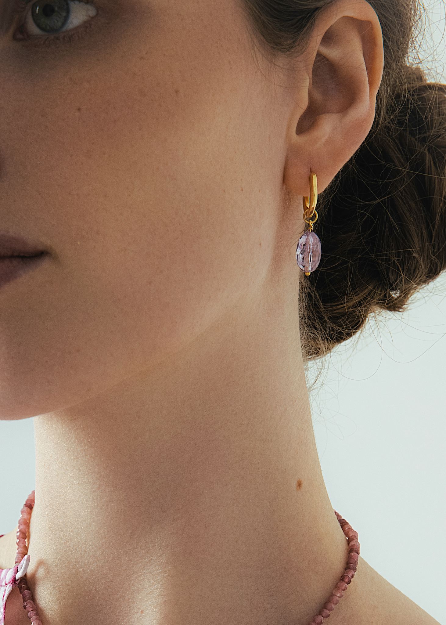 Kvinde med hængeøreringe i guld med twist hoops og et charm med ametyst ædelsten i facetslebne 