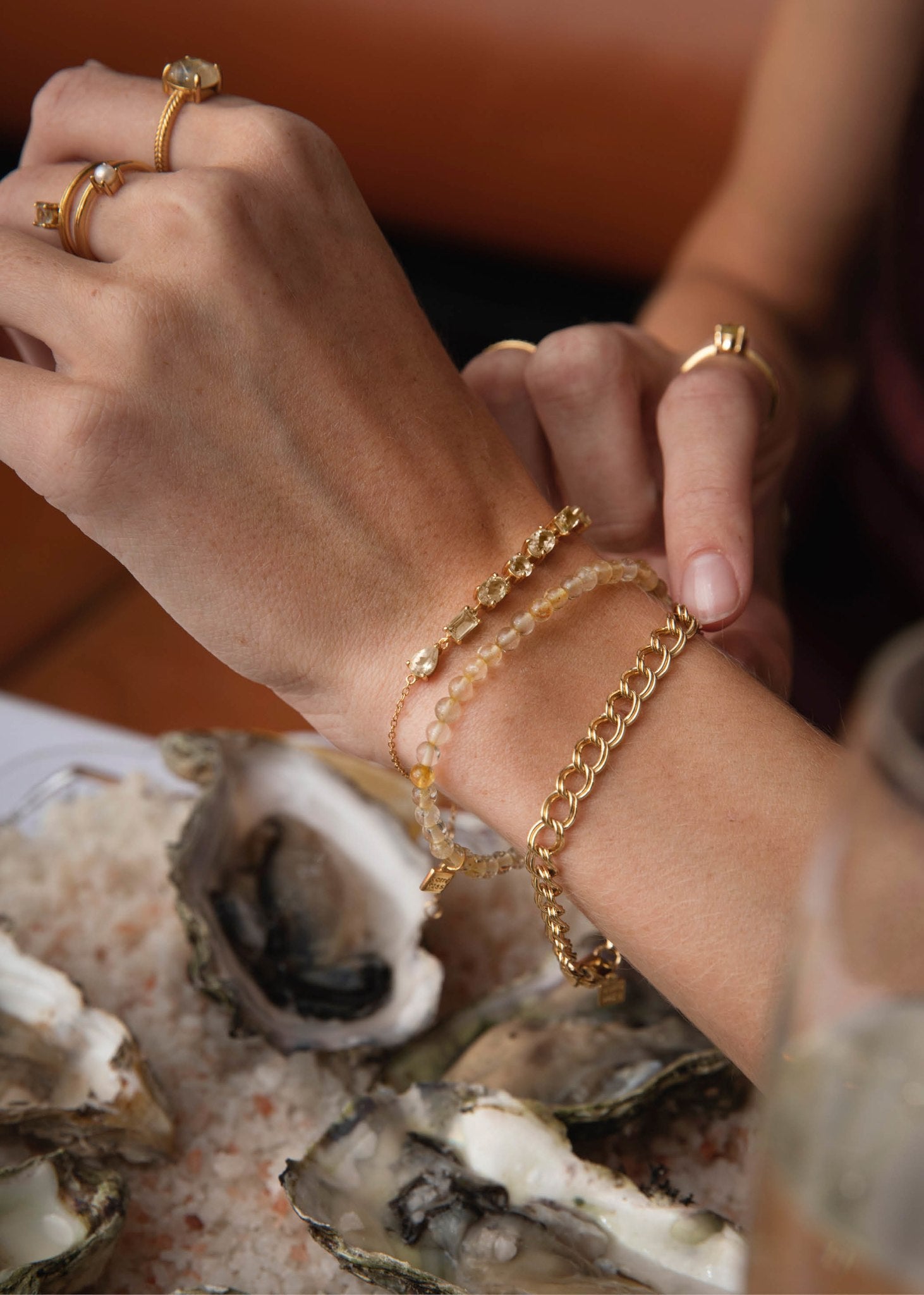 Kvindehånd med forskellige armbånd fra carré jewellery, to med ædelsten og et chunky guld dobbelt rombo armbånd
