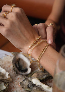 Kvindehånd med forskellige armbånd fra carré jewellery, to med ædelsten og et chunky guld dobbelt rombo armbånd