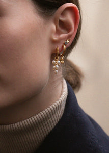 Kvinde med hoops og charms i guldbelagt sølv fra carré jewellery med lange hængeøreringe i guld med ferskvandsperler