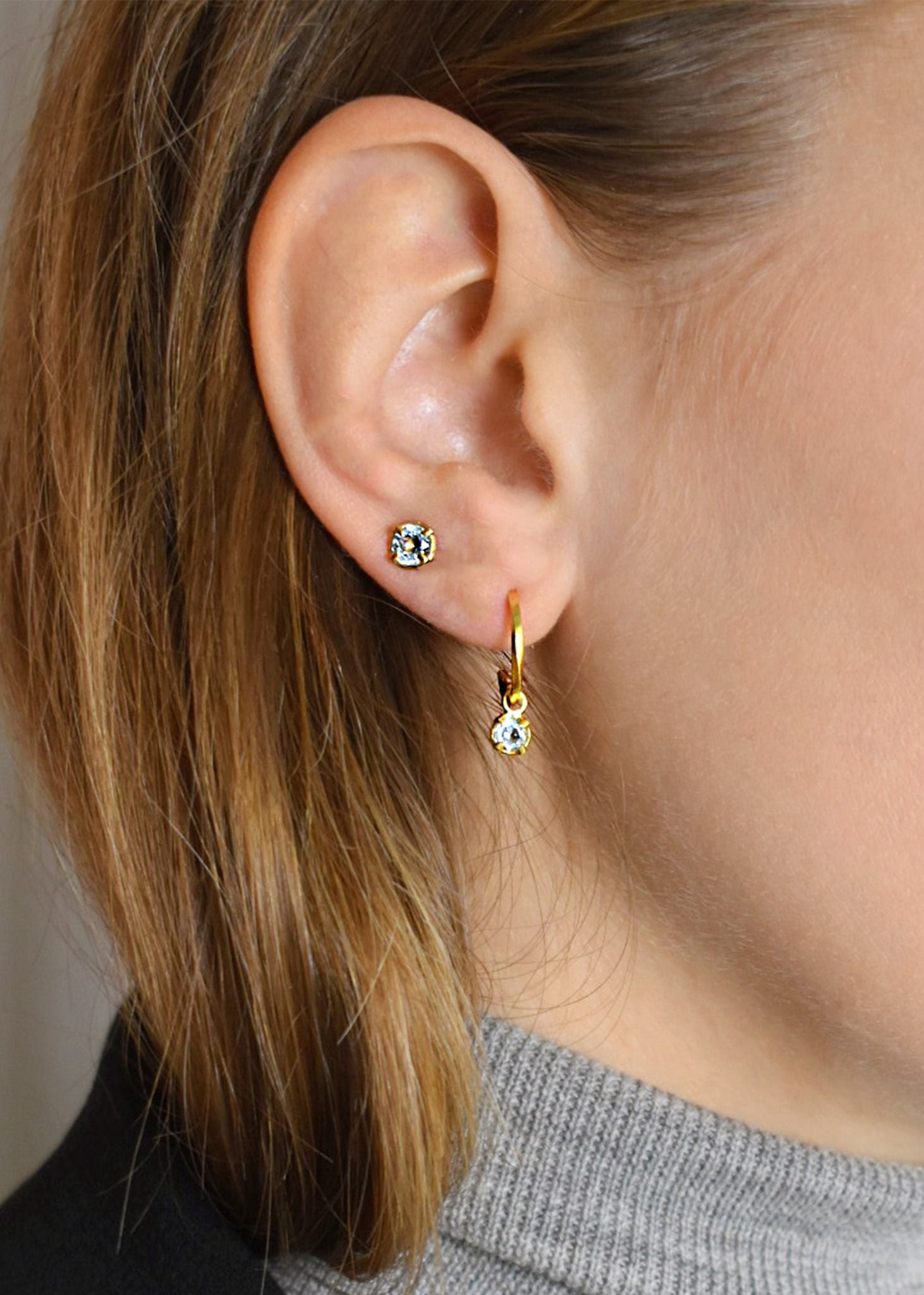 Ung kvinde med små ørestikker i guldbelagt sølv med november måneds fødselssten, blå topas