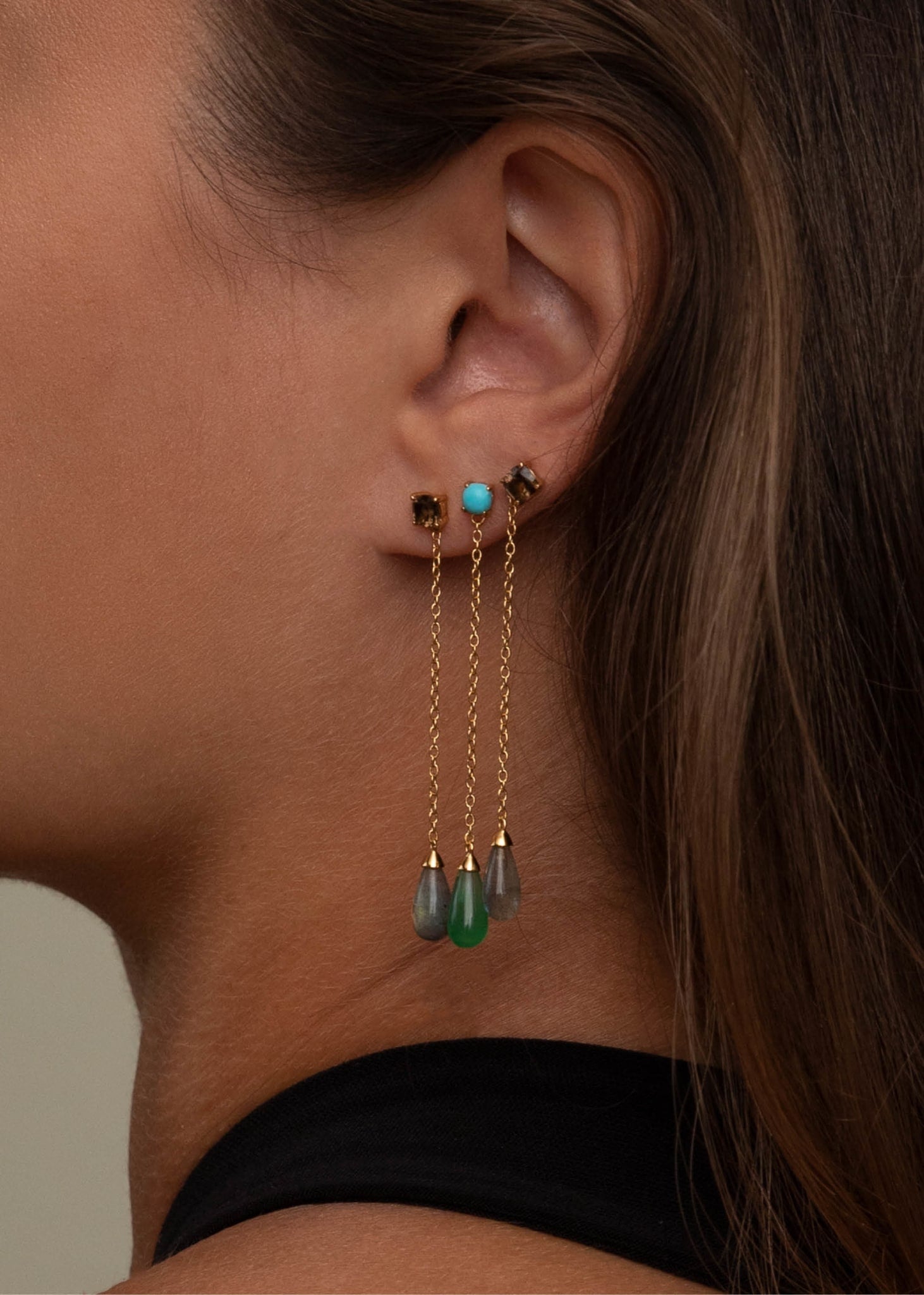 Kvinde med lange øreringe fra Carré Jewellery med grønne, blå, grå og brune sten og lange guldkæder ørestikker