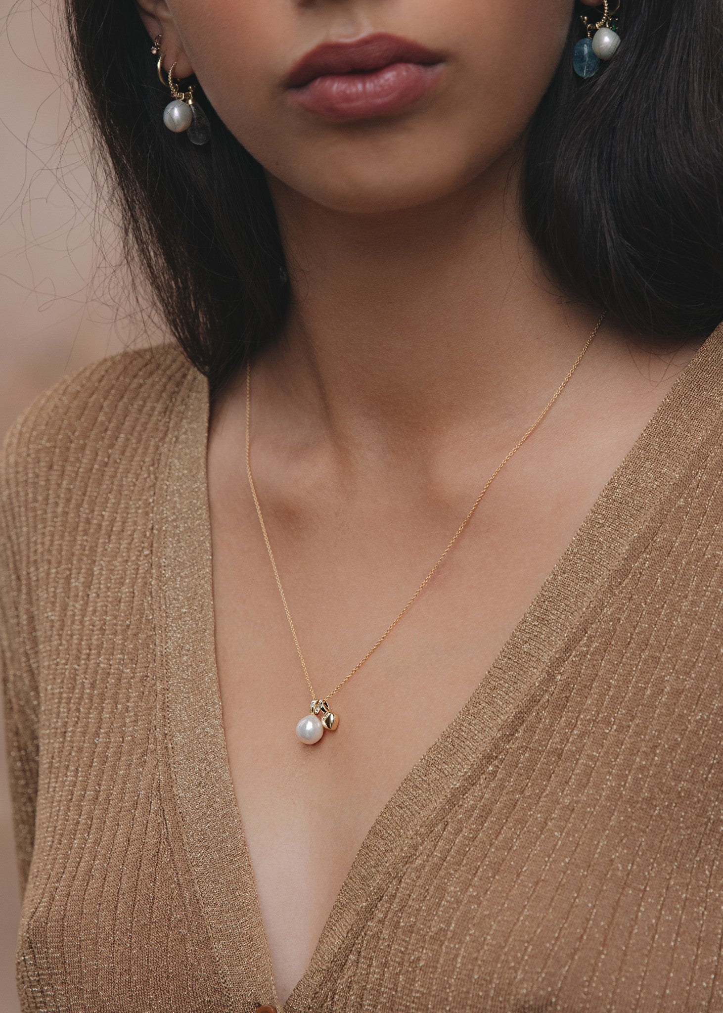 Kvinde med en halskæde i ægte guld fra carré jewellery med et hjertevedhæng i guld og et ferskvandsperle vedhæng i guld med en blå safir i øksenet
