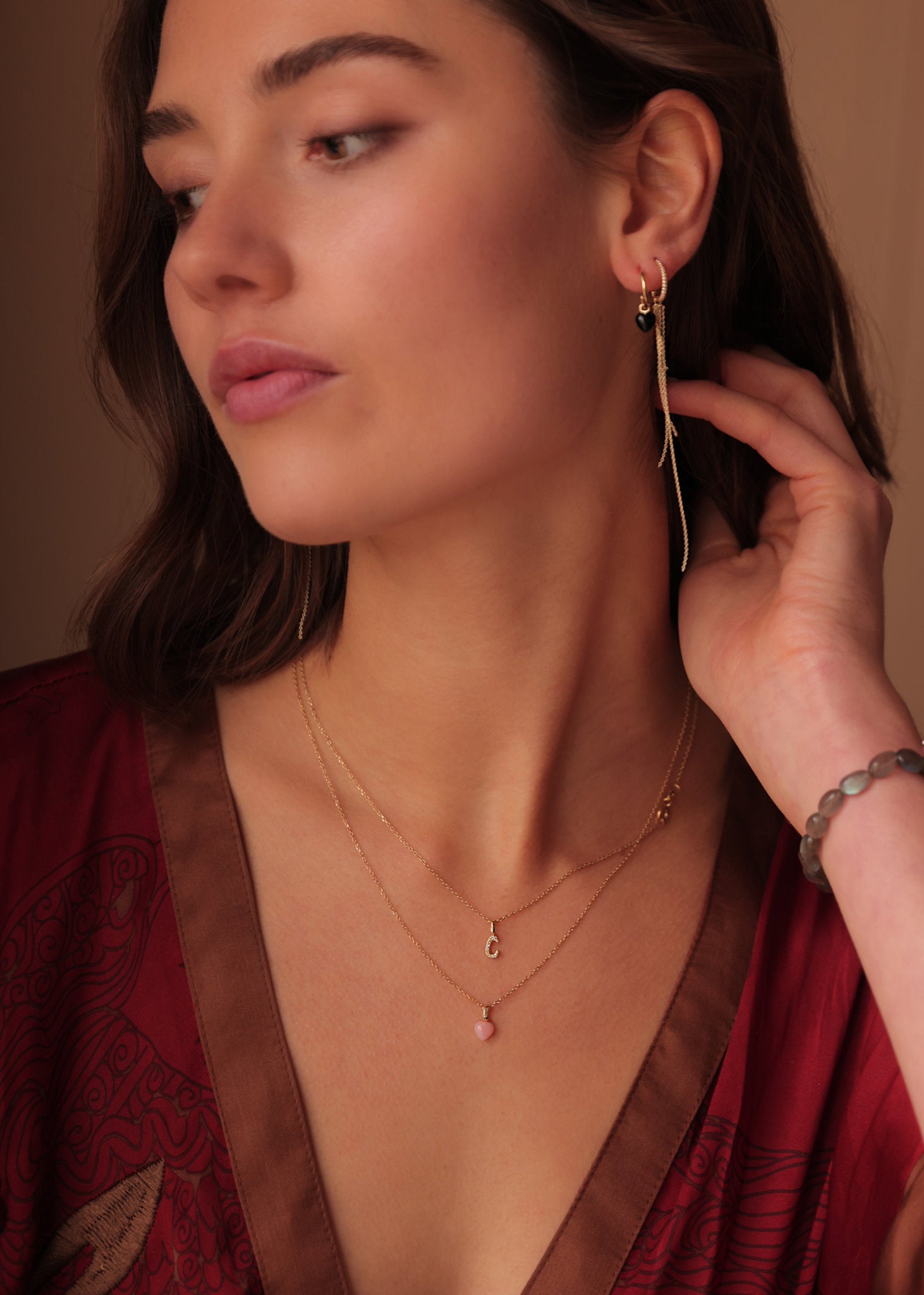 Kvinde med ægte guldsmykker i 10-karat guld fra carré jewellery med et hjerteformet vedhæng til halskæder med pink opal og diamant og et bogstavsvedhæng i bogstavet c med diamanter