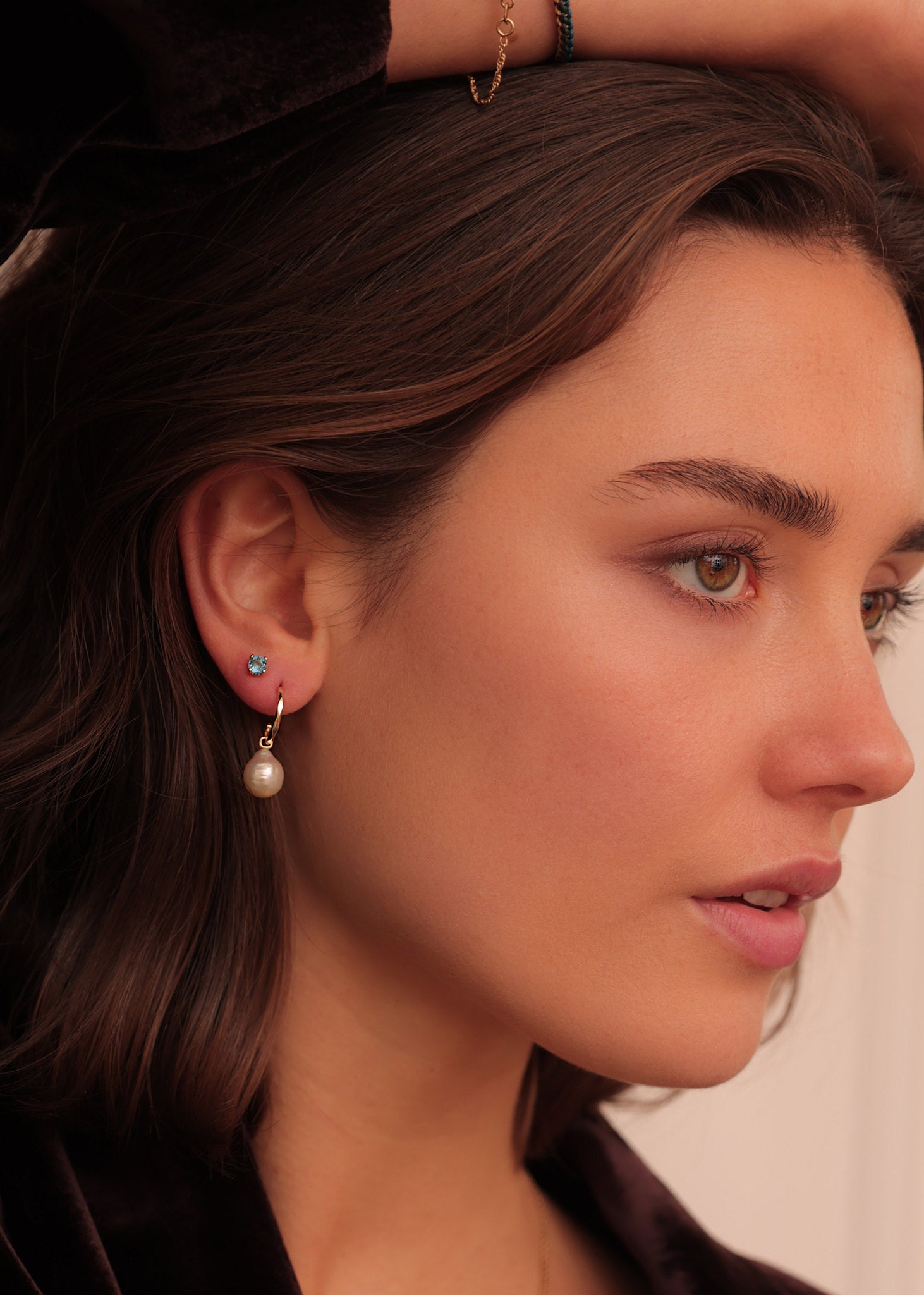 Kvinde med 10-karat øreringe fra Carré Jewellery i ægte guld med en stor hvid ferskvandsperle og en enkelt ørestik i guld med london blå topas