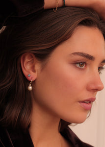 Kvinde med 10-karat øreringe fra Carré Jewellery i ægte guld med en stor hvid ferskvandsperle og en enkelt ørestik i guld med london blå topas