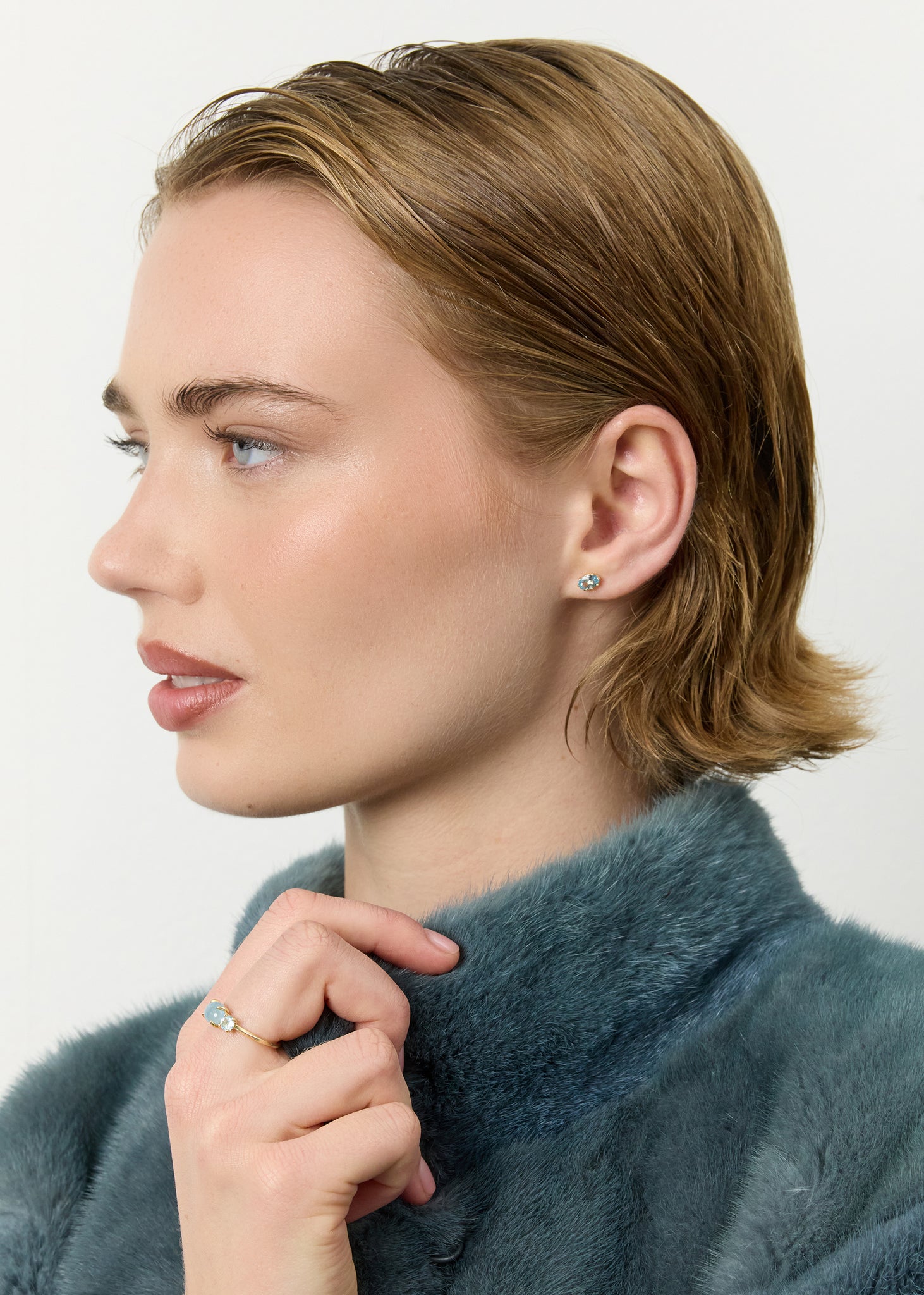 ung kvinde med små ørestikker i 10k ægte guld med en facetslebet blå topas ædelsten og en trestens ring i 10k guld med akvamarin og blå topas ædelsten