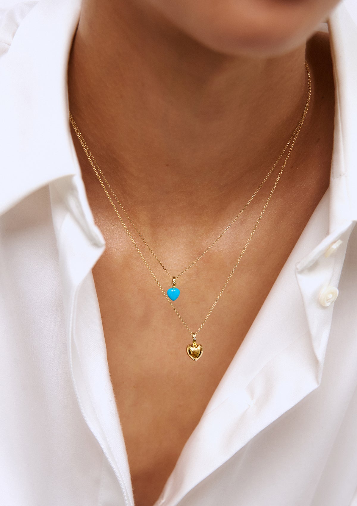 En kvinde med to guld hjertevedhæng fra carré. Den øverste hjerte halskæde har et turkis hjerte med en diamant og det nedeste er et hjerte i solidt guld med en diamant